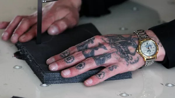 Two tattooed hands are sewing a piece of cloth